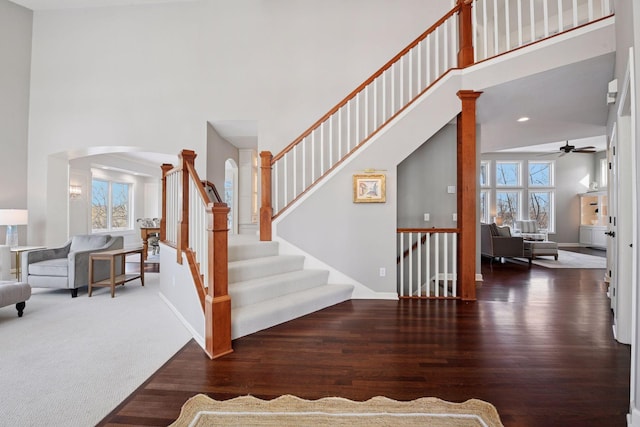 stairway featuring wood finished floors, baseboards, decorative columns, arched walkways, and a towering ceiling