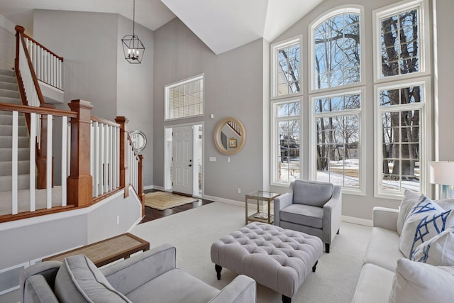 carpeted living area featuring stairs, a notable chandelier, plenty of natural light, and baseboards