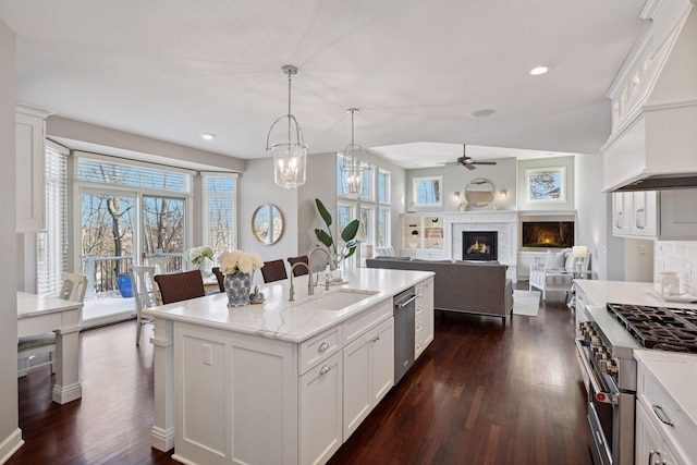 kitchen with dark wood finished floors, a warm lit fireplace, appliances with stainless steel finishes, and a sink