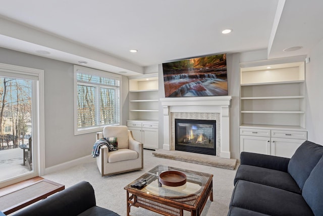 living area with built in features, a glass covered fireplace, recessed lighting, baseboards, and light colored carpet