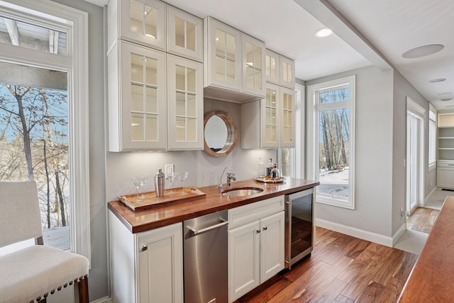 kitchen with wooden counters, a sink, wood finished floors, wine cooler, and baseboards