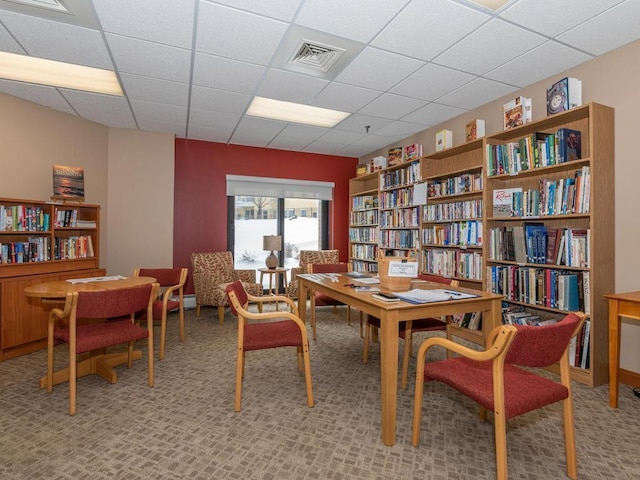 living area with a drop ceiling and light carpet