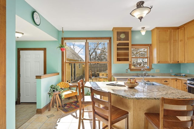 kitchen with a kitchen island, sink, a kitchen bar, light tile patterned floors, and light stone countertops