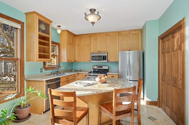 kitchen with sink, light tile patterned floors, appliances with stainless steel finishes, a kitchen island, and light stone countertops