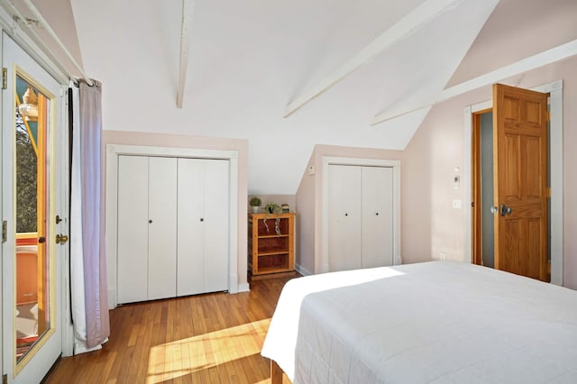 bedroom featuring lofted ceiling with beams, light hardwood / wood-style floors, and multiple closets