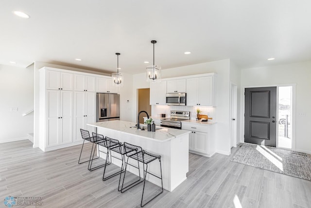 kitchen featuring an island with sink, light hardwood / wood-style floors, a kitchen bar, white cabinets, and appliances with stainless steel finishes