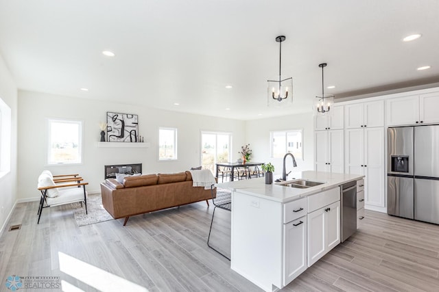 kitchen featuring white cabinets, appliances with stainless steel finishes, a center island with sink, and a healthy amount of sunlight