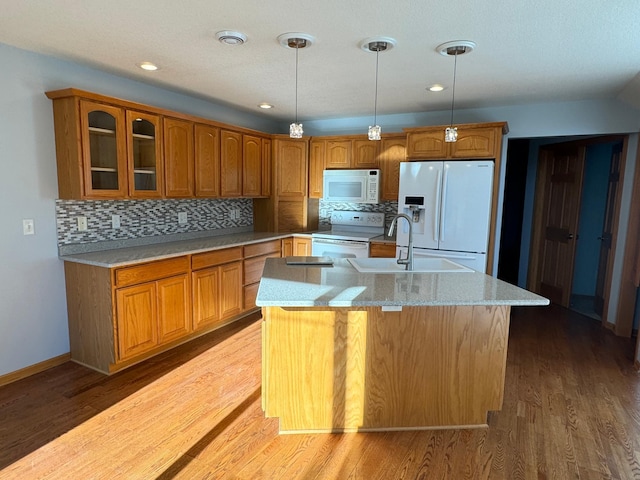 kitchen with white appliances, backsplash, a kitchen island with sink, hanging light fixtures, and light hardwood / wood-style flooring