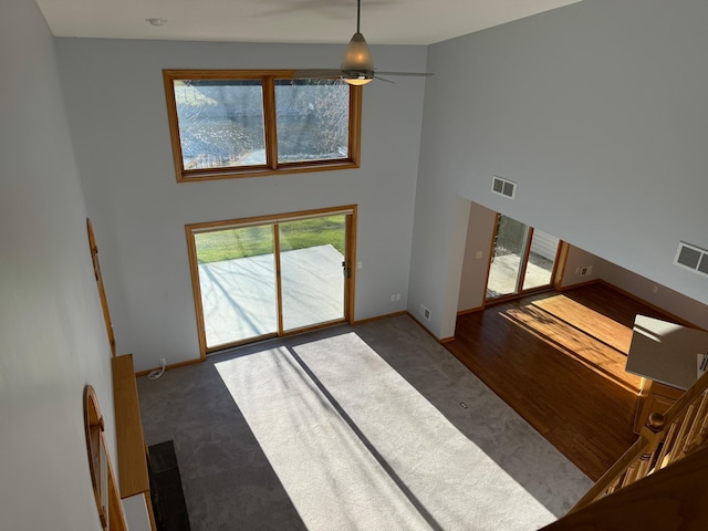 unfurnished living room featuring ceiling fan, plenty of natural light, dark wood-type flooring, and a high ceiling