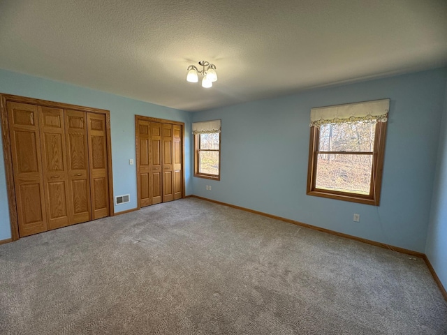 unfurnished bedroom featuring a textured ceiling, light carpet, and two closets