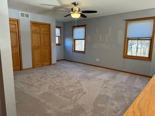 spare room with a textured ceiling, light colored carpet, ceiling fan, and a healthy amount of sunlight