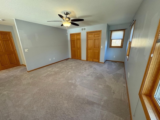 unfurnished bedroom with two closets, ceiling fan, light colored carpet, and a textured ceiling