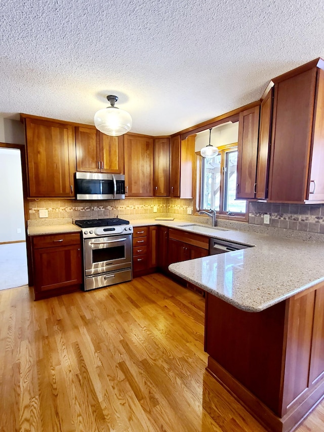 kitchen featuring pendant lighting, sink, light hardwood / wood-style flooring, appliances with stainless steel finishes, and kitchen peninsula