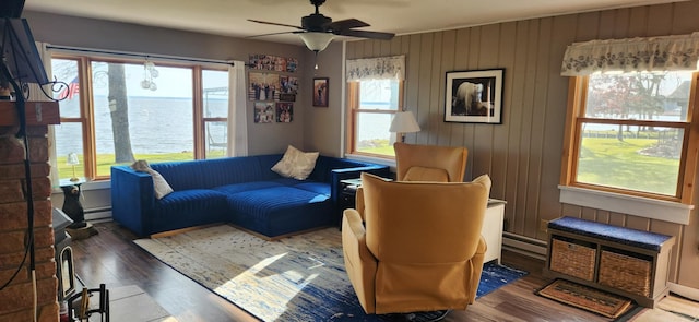 living room with dark hardwood / wood-style flooring, ceiling fan, a baseboard heating unit, a water view, and wood walls