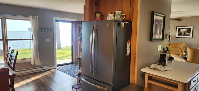 kitchen featuring baseboard heating, wooden walls, dark wood-type flooring, a water view, and stainless steel refrigerator