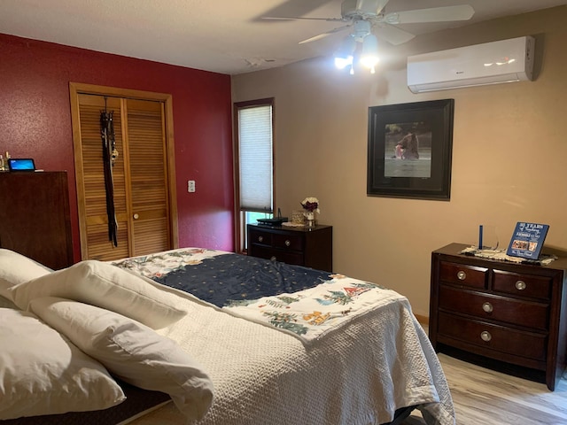 bedroom featuring ceiling fan, a closet, a wall mounted air conditioner, and light wood-type flooring