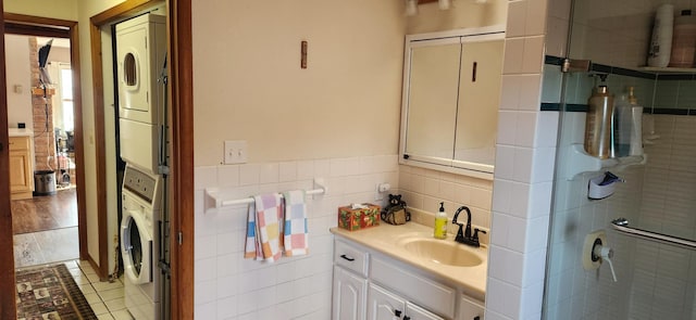 bathroom with stacked washer and clothes dryer, hardwood / wood-style floors, an enclosed shower, vanity, and tile walls