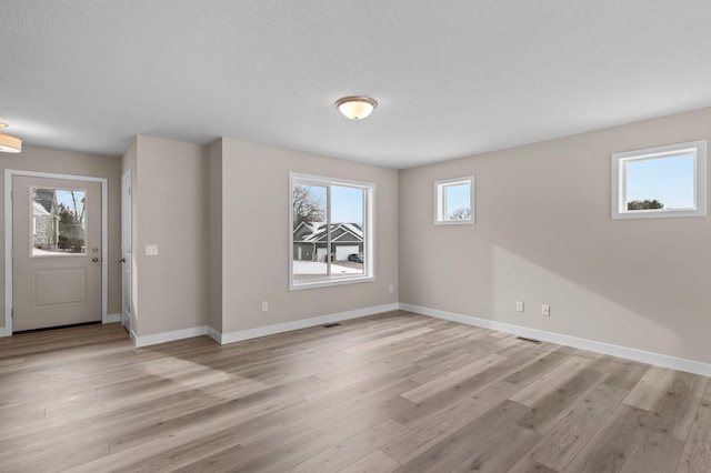 interior space with light wood-type flooring, visible vents, a textured ceiling, and baseboards