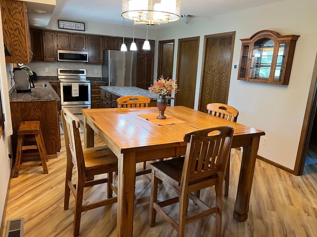 dining space with a textured ceiling, a notable chandelier, sink, and light hardwood / wood-style flooring