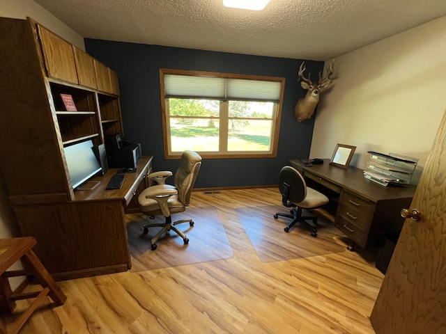 home office with light wood-type flooring and a textured ceiling