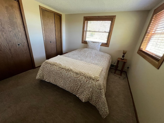 bedroom featuring dark carpet, a textured ceiling, and multiple closets