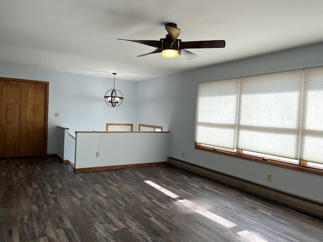 unfurnished room with ceiling fan with notable chandelier, dark wood-type flooring, and a baseboard heating unit