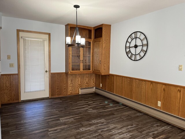 unfurnished dining area featuring a notable chandelier, dark hardwood / wood-style floors, wooden walls, and a baseboard heating unit