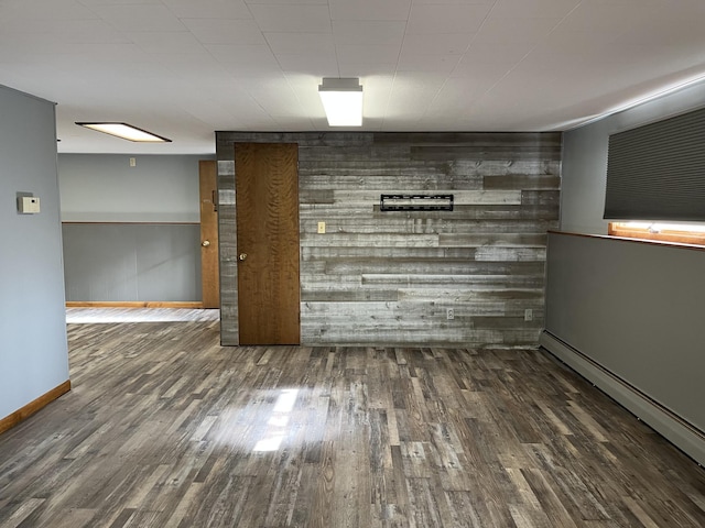 basement with dark hardwood / wood-style flooring, wooden walls, and a baseboard heating unit