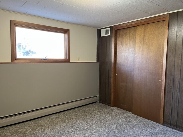 unfurnished bedroom featuring carpet, a baseboard radiator, a closet, and wood walls