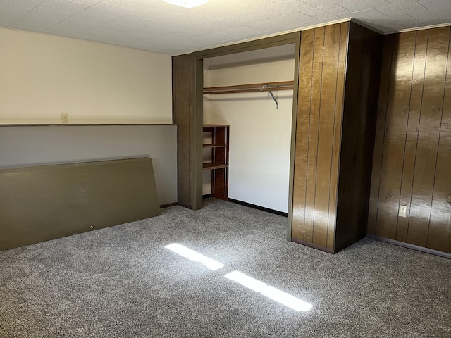 unfurnished bedroom with carpet, wood walls, and a closet