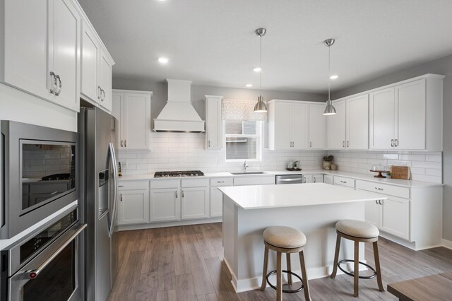 kitchen with appliances with stainless steel finishes, premium range hood, white cabinetry, and hanging light fixtures