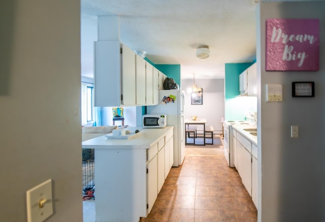 kitchen featuring decorative light fixtures, white appliances, white cabinetry, and an inviting chandelier