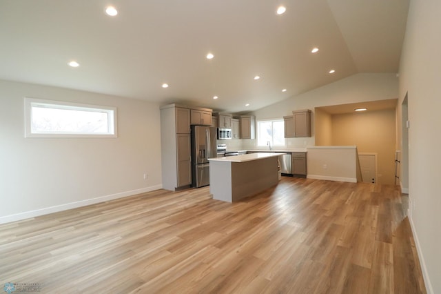 kitchen with lofted ceiling, sink, light hardwood / wood-style flooring, appliances with stainless steel finishes, and a kitchen island