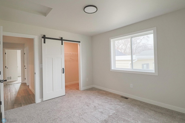 unfurnished bedroom with a barn door, a spacious closet, carpet floors, and a closet