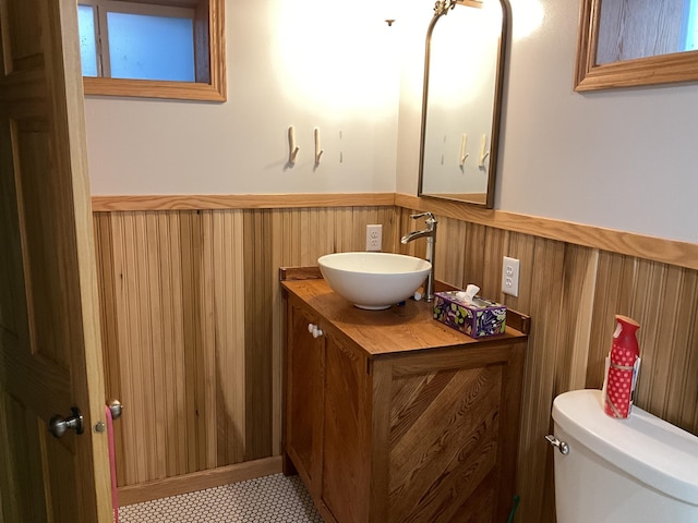 bathroom featuring tile patterned floors, vanity, toilet, and wooden walls