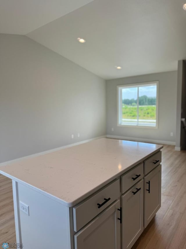 kitchen with light stone counters, light hardwood / wood-style floors, vaulted ceiling, gray cabinets, and a kitchen island