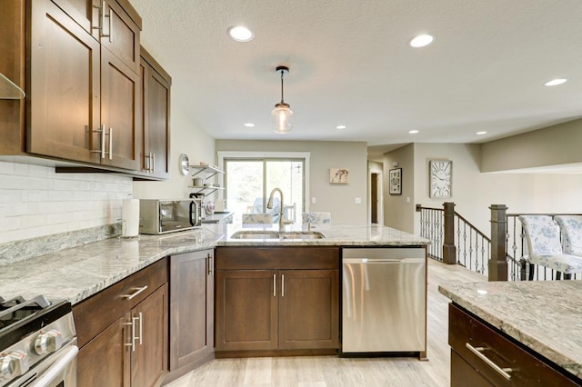 kitchen featuring light stone countertops, appliances with stainless steel finishes, decorative backsplash, sink, and hanging light fixtures