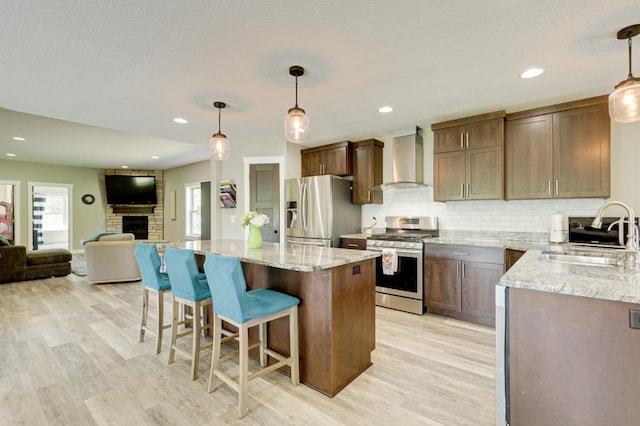 kitchen featuring stainless steel appliances, hanging light fixtures, wall chimney exhaust hood, and sink