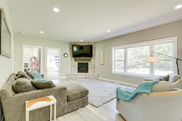 living room with a stone fireplace, a textured ceiling, and light hardwood / wood-style flooring