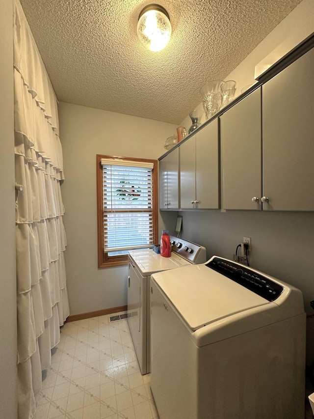 washroom featuring a textured ceiling, cabinet space, light floors, and washer and clothes dryer