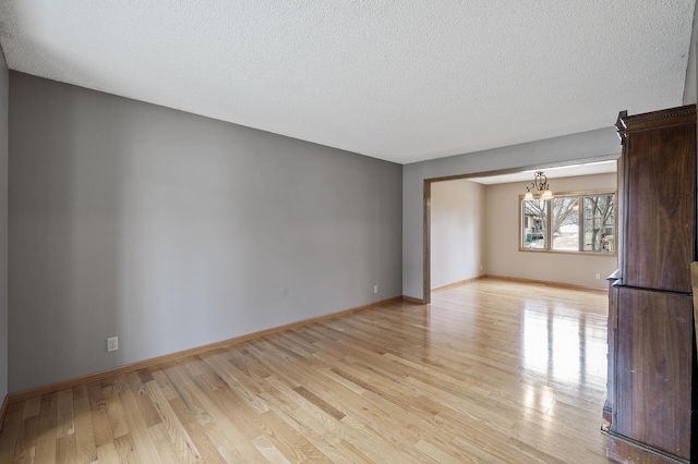 unfurnished living room with light hardwood / wood-style floors, a textured ceiling, and a notable chandelier