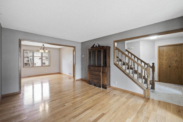 unfurnished living room featuring a chandelier, light hardwood / wood-style floors, and a textured ceiling