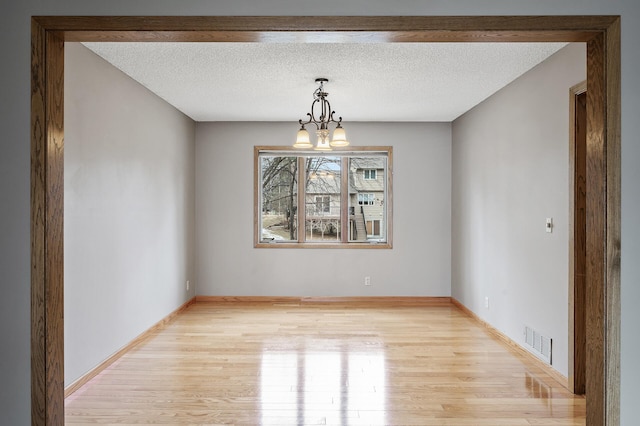 unfurnished dining area featuring an inviting chandelier, light hardwood / wood-style flooring, and a textured ceiling