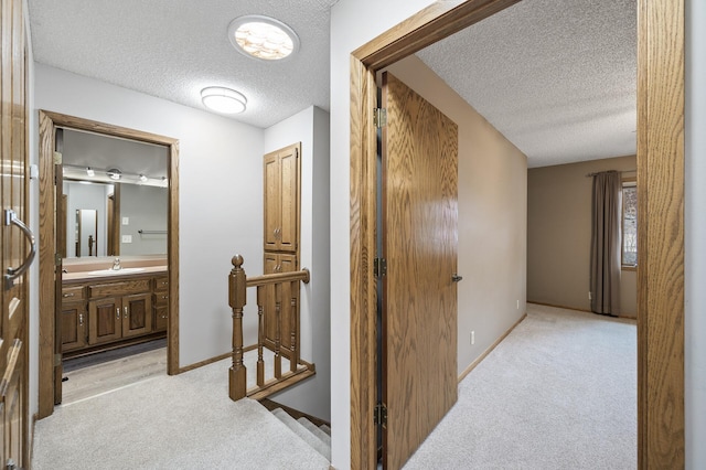 corridor with sink, light colored carpet, and a textured ceiling