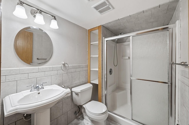 bathroom featuring a shower with door, sink, tile walls, and toilet