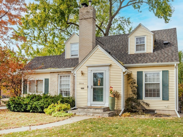 new england style home featuring a chimney, a front lawn, and roof with shingles