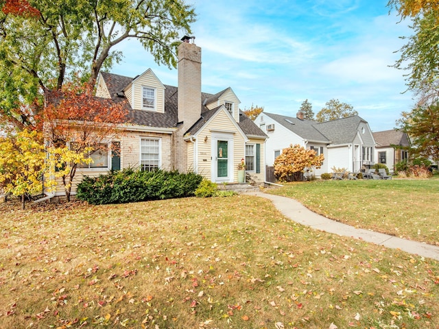 cape cod house featuring a front yard, roof with shingles, and a chimney