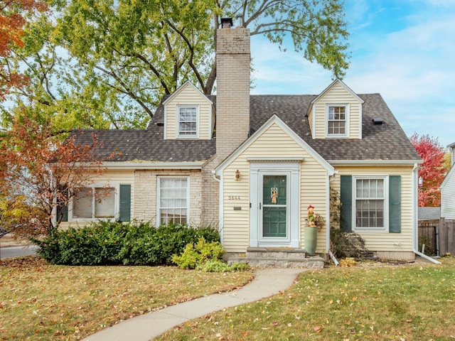 cape cod home with a front yard, roof with shingles, fence, and a chimney