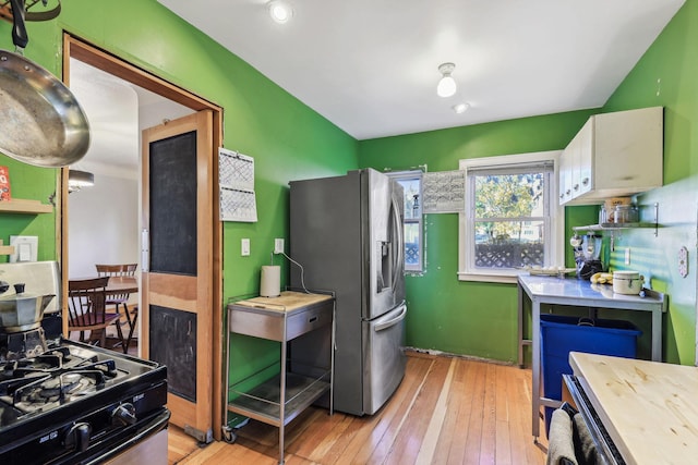 kitchen featuring light wood-type flooring, white cabinets, black gas range, and stainless steel fridge with ice dispenser