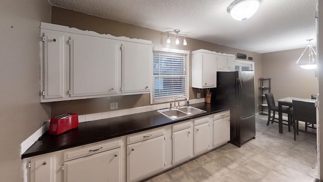 kitchen featuring black fridge, a textured ceiling, white cabinetry, and sink